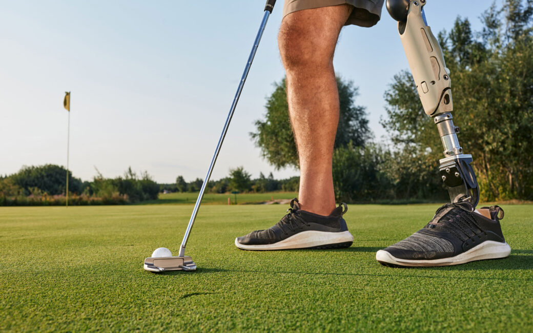 Professional golfer with prosthetic leg hitting with putter on golf ball during golfing. Concept of