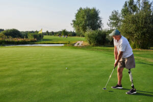A golfer with a prosthetic leg prepares to putt on the green amidst the lush landscape and clear.